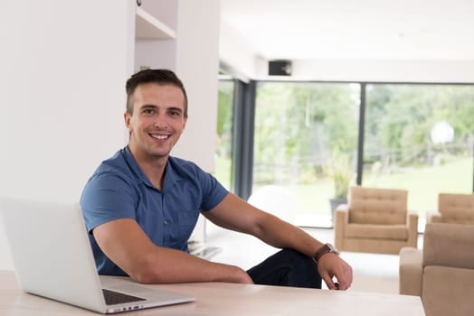 Young man with his laptop computer at his luxury modern home, smiling