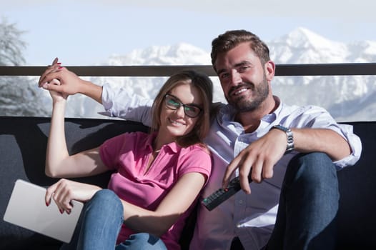 Young couple sitting on sofa near the window watching television together at luxury home