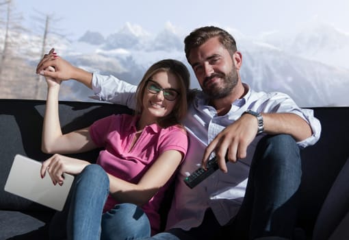 Young couple sitting on sofa near the window watching television together at luxury home