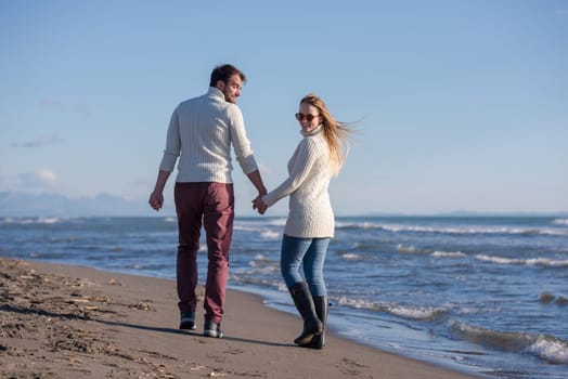Young couple having fun walking and hugging on beach during autumn sunny day