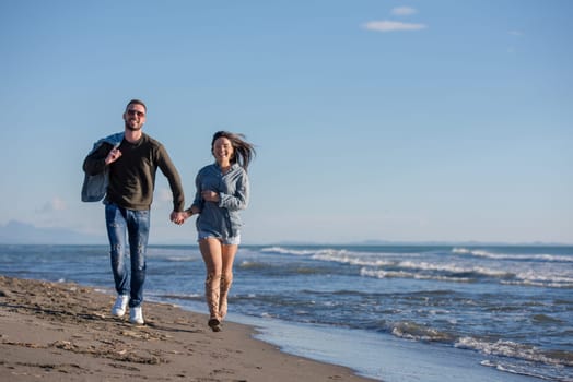 Young couple having fun walking and hugging on beach during autumn sunny day