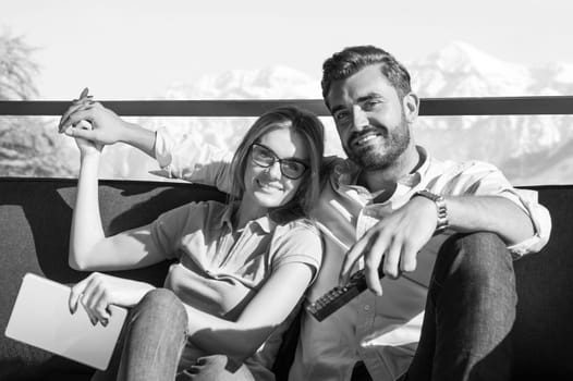 Young couple sitting on sofa near the window watching television together at luxury home