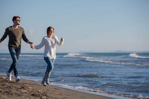 Young couple having fun walking and hugging on beach during autumn sunny day