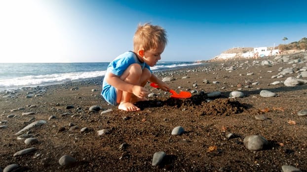 Cute little boy digging sand on the sea ocean beach and building sand castle.