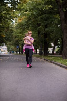 young sporty mother carries little daughter in arms while jogging in a city park,outdoor sports and fitness