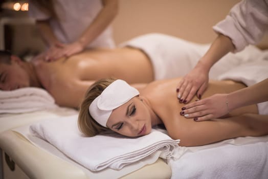 Relaxed young beautiful couple receiving a back massage from masseur in a spa