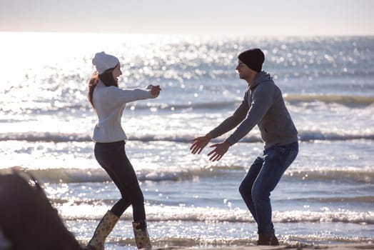 Young couple having fun walking and hugging on beach during autumn sunny day