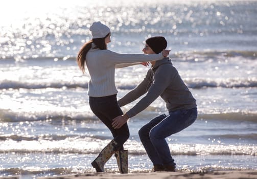Young couple having fun walking and hugging on beach during autumn sunny day
