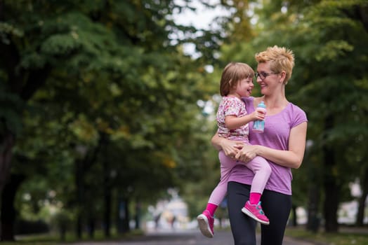 young sporty mother carries little daughter in arms while jogging in a city park,outdoor sports and fitness
