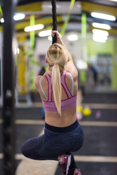 young muscular woman doing rope climbing in cross fitness gym