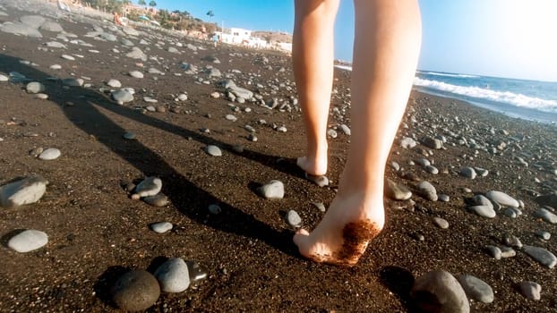 Closeup rear view image of sexy female feet walking away on the sea beach with black volcanic sand.