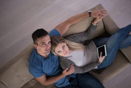 Young couple sitting on a sofa in the luxury living room, using a tablet computer top view