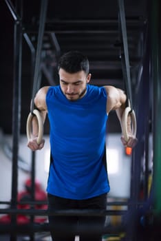 young athlete man working out pull ups with gymnastic rings at the cross fitness gym