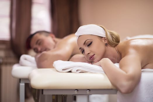 Portrait of relaxed beautiful young couple lying on massage table at spa center