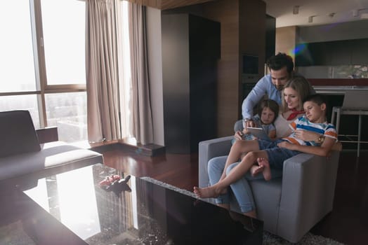 happy couple spending time with kids using tablet computer on an armchair  at home