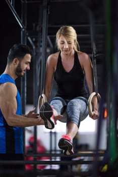 young athletic woman working out with personal trainer on gymnastic rings at the cross fitness gym