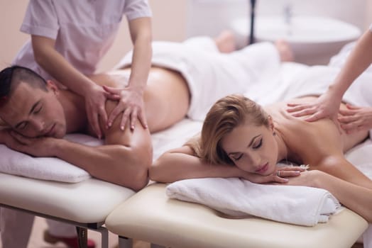 Relaxed young beautiful couple receiving a back massage from masseur in a spa