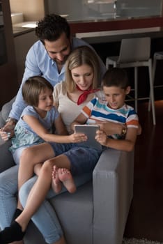 happy couple spending time with kids using tablet computer on an armchair  at home