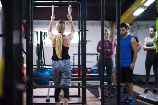 young athletic woman working out with personal trainer on gymnastic rings at the cross fitness gym