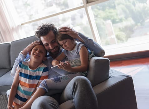 happy father spending time with kids using tablet computer on an armchair  at home