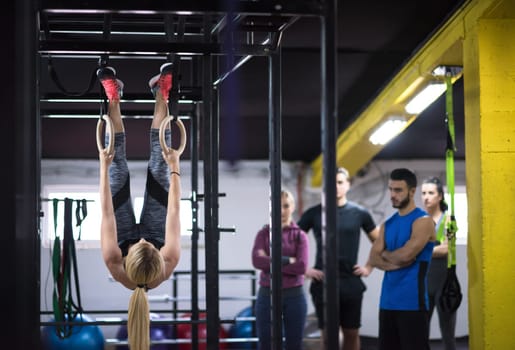 young athletic woman working out with personal trainer on gymnastic rings at the cross fitness gym