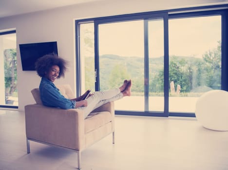 Young african american woman at home relaxing in her luxury lliving room reading a digital tablet PC surf internet and work