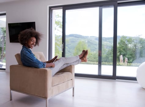 Young african american woman at home relaxing in her luxury lliving room reading a digital tablet PC surf internet and work