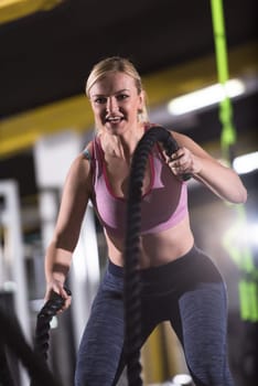 young fit athlete woman working out in functional training gym doing  battle ropes exercise as part of cross fitness training