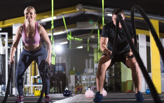 young fit sports couple working out in functional training gym doing  battle ropes cross fitness exercise