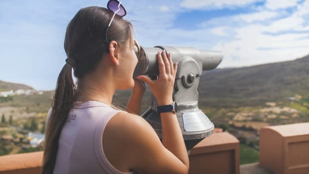 Toned portrait of female tourist using coin operated binoculars on high mountain observation deck.