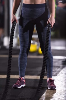 young fit athlete woman working out in functional training gym doing  battle ropes exercise as part of cross fitness training