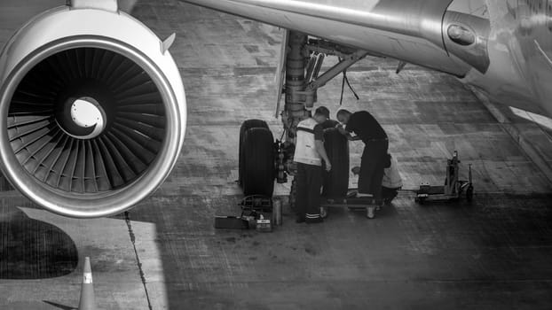 Black and white image of maintenance ground crew checking and repairing airplane chassis wheels before taking off.