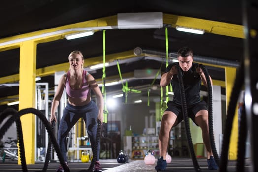 young fit sports couple working out in functional training gym doing  battle ropes cross fitness exercise