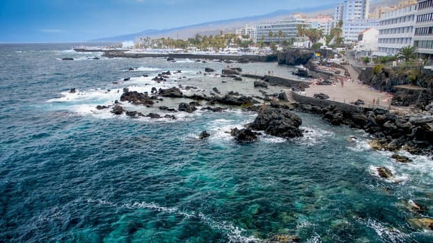 Beautiful view on ocean waves breaking on volcanic cliffs at seaside city.