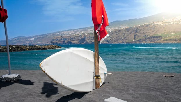 White surfboard and lifeguard post on the ocean beach wth black volcanic sand.