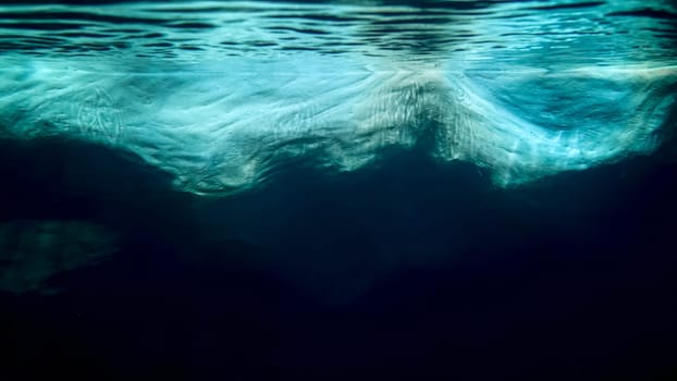 Underwater photo of big iceberg floating in cold ocean water.