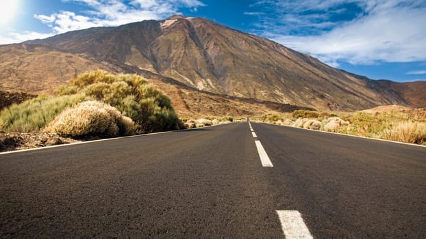 Long empty highway road in the desert going to mountains. Road to volcano Teide, Tenerife, Spain.