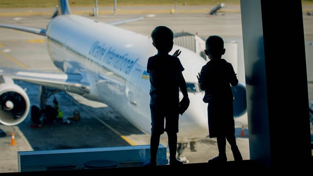 Silhouette of two little boys loking through window on airplane in airport terminal.