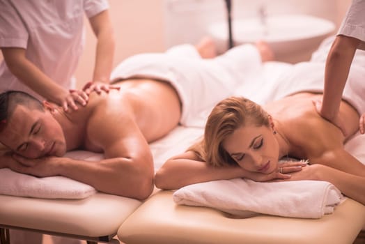 Relaxed young beautiful couple receiving a back massage from masseur in a spa