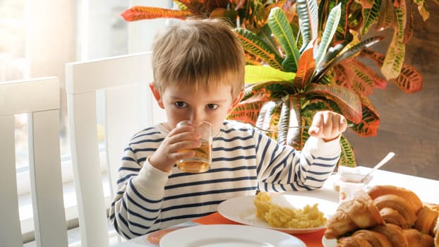 Portrait of cute little boy drinkin gjuice while having reakfast in dining room.