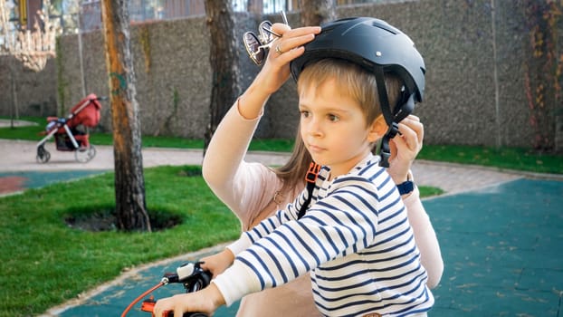Closeup photo of young mother wearing protective helmet on her son before riding a bicycle.
