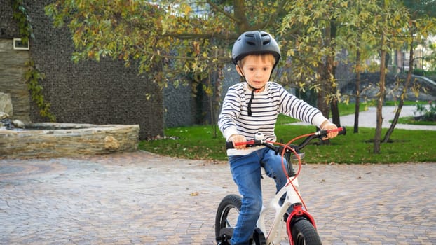 Adorable toddler boy in safety helmet riding bicycle for first time.