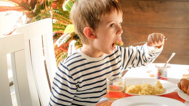 Portrait of little toddler boy eating scrambled eggs with fork for breakfast.
