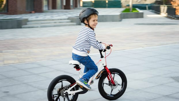 Happy smiling boy riding fast his bicycle on city street.