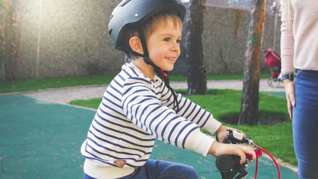 Toned portrait of cheerful smiling little boy in black protective helmet riding his bicycle.