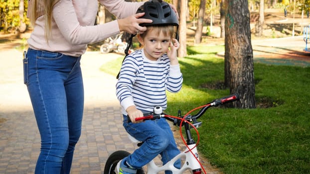 Closeup photo of young caring woman putting on protective helmet on her son riding a bicycle.