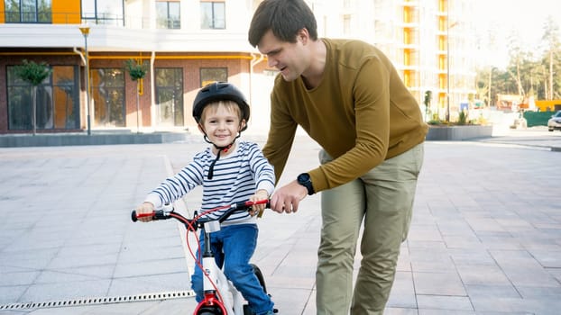 Portrait of smiling little boy learning riding his first bicycle with young father.