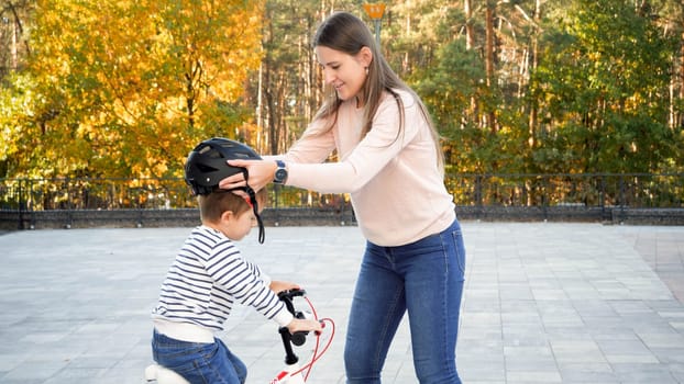 Portrait of beautiful young woman putting protective helmet on her son before teaching riding a bicycle.