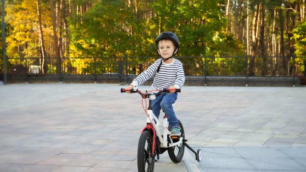 Happy little boy in helmet enjoying riding bicycle at park.