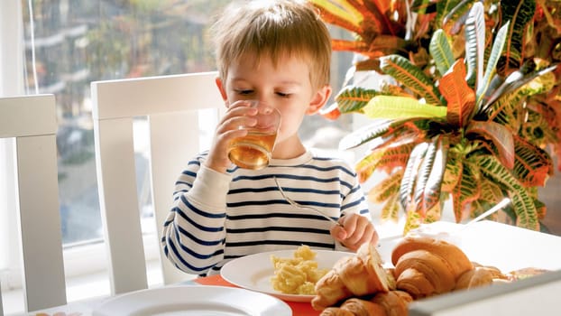 Cute 3 years old boy drinking apple juice from glass during dinner in dining room.